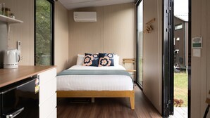 A bedroom with a bed, a coffee maker, an air conditioner, and a view of the outdoors.