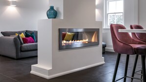 Un salon moderne avec une cheminée intégrée, un canapé gris agrémenté de coussins colorés et un tabouret de bar rouge.