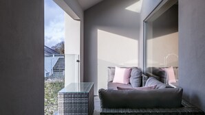 Un balcon moderne avec une table en verre, un canapé confortable et une vue sur une maison.