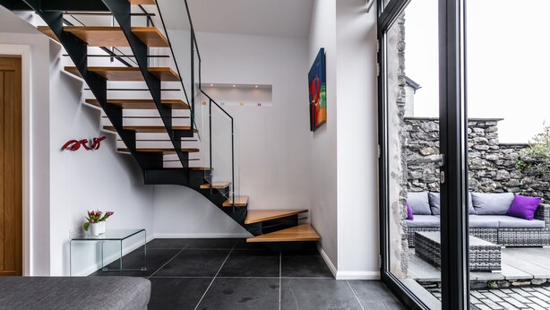 Un intérieur moderne avec un escalier noir, une table basse en verre et une vue sur un espace extérieur aménagé en salon.