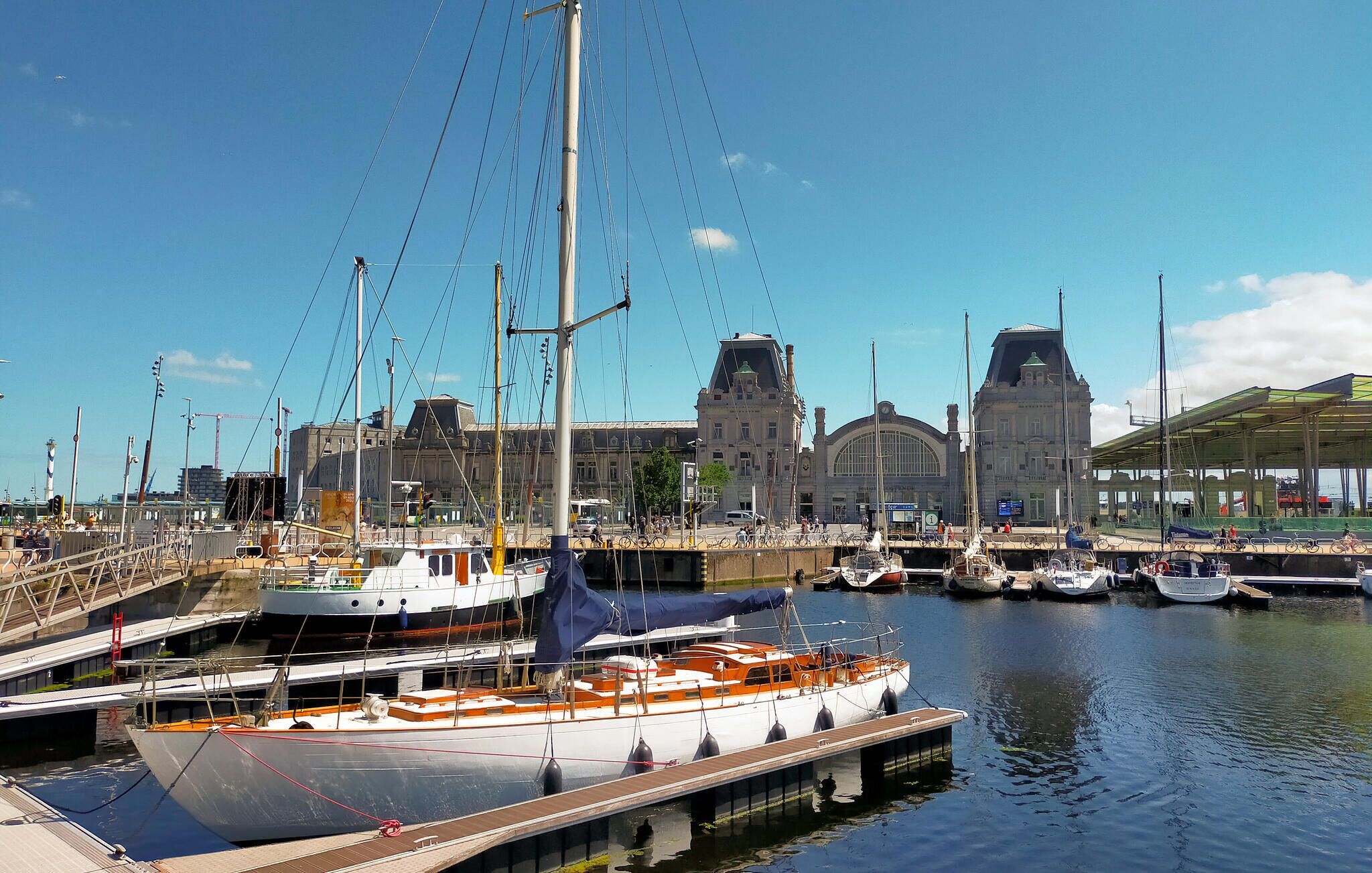 Un port de plaisance avec des bateaux amarrés, un grand bâtiment doté d’un clocher et un ciel bleu dégagé.