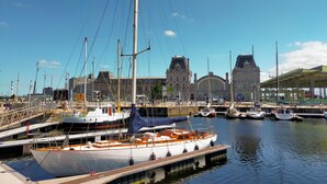 A marina with boats docked, a large building with a clock tower, and a clear blue sky.