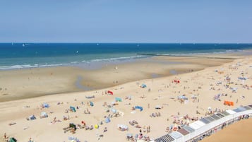 Une vaste plage parsemée de nombreux transats et parasols, un ciel dégagé et une mer calme.