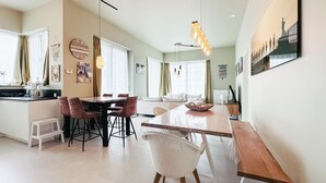 A modern kitchen with a dining area, featuring a large wooden table, chairs, and a hanging light fixture.
