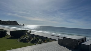 Una terraza de madera con vistas al océano y un litoral rocoso lejano.