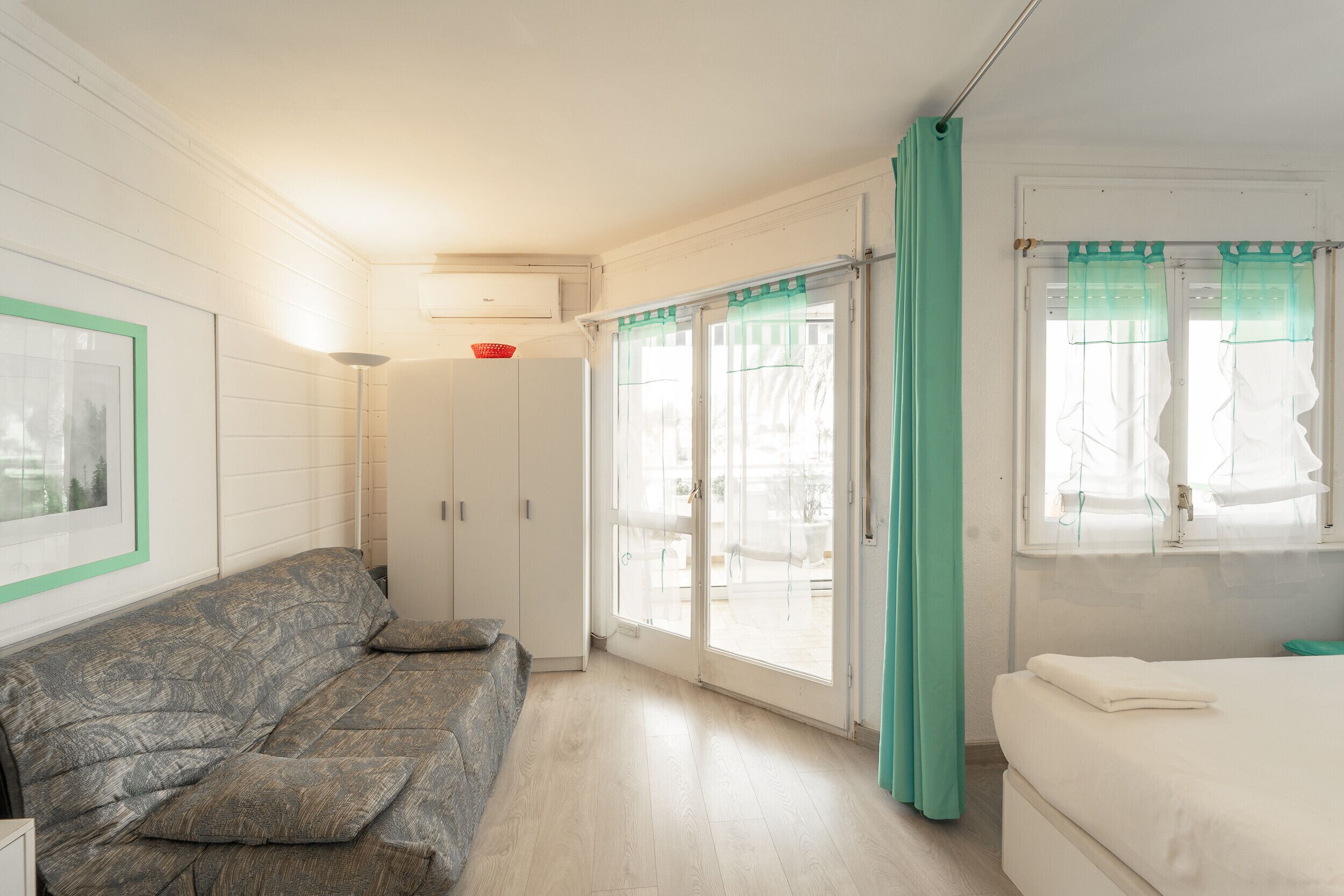 A room with a sofa, a bed, a window with curtains, and a door leading to an outdoor area.