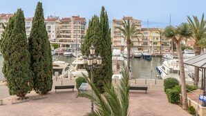 Een jachthaven met aangemeerde boten, omgeven door hoge cipressen en palmbomen, met gebouwen op de achtergrond.