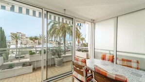 Een balkon met een tafel en stoelen, bloempotten en uitzicht op palmbomen en gebouwen.