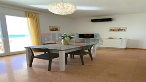 A modern living room with a dining table, chairs, a large window with curtains, a ceiling light fixture, a flat-screen TV, and a small cabinet. - Vacation home La Perla Salentina (Marina di Capilungo)
