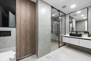 A modern bathroom with a glass-enclosed shower, a wooden panel, and a white vanity with a black sink. - Newly Upgraded Elegant 1 BD Apartment (Dubai)