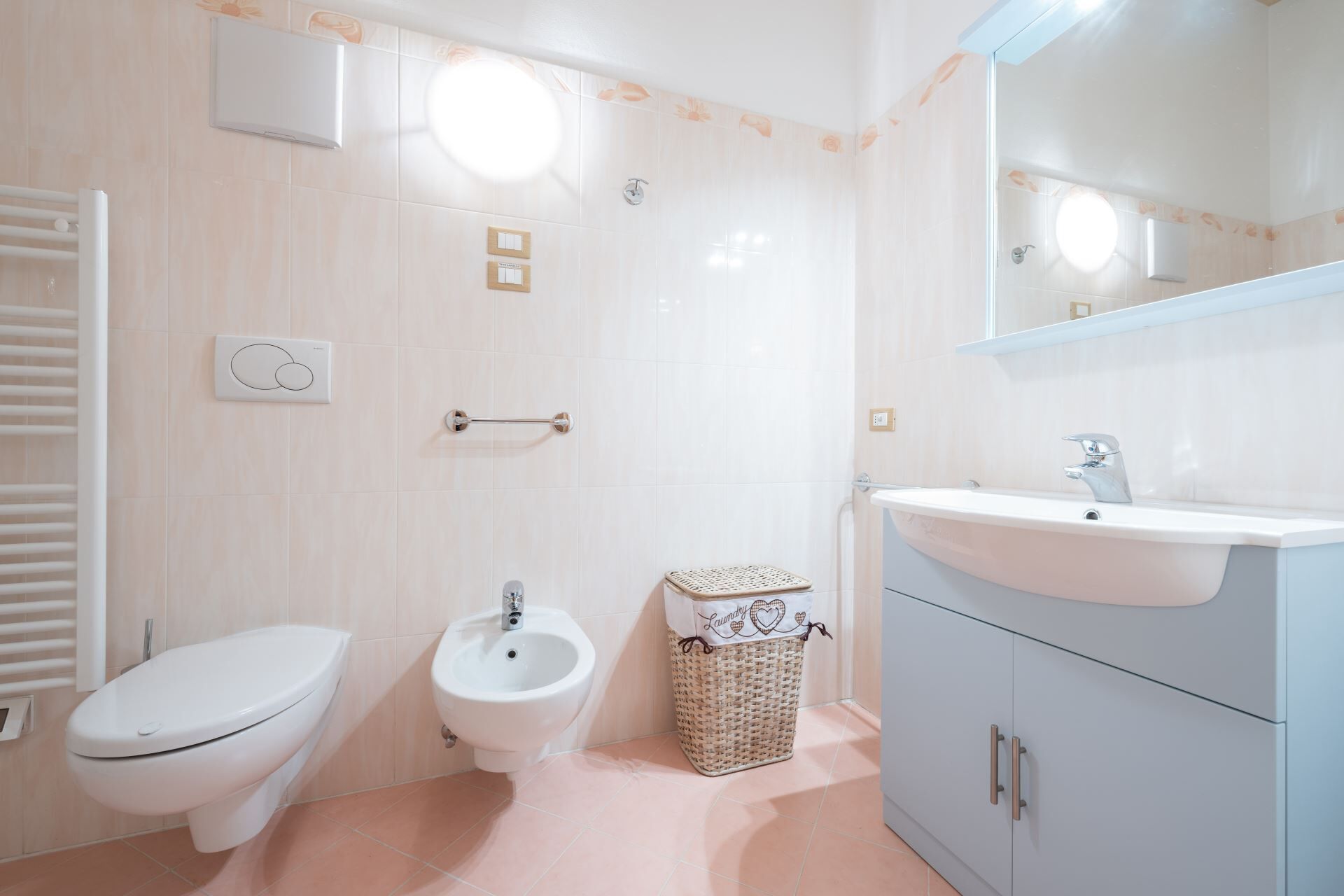 A bathroom with a toilet, bidet, vanity with a sink, and a mirror.