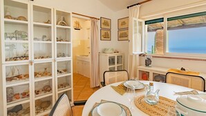 Un comedor con una mesa redonda dispuesta para cuatro personas, rodeada de sillas de mimbre. Un armario blanco con puertas de vidrio exhibe diversos objetos decorativos.