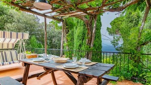 An outdoor dining area with a wooden table set for four, surrounded by a pergola and a view of a lake.