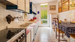 A kitchen with white cabinets, a stove, and a sink. There is a window with a view of greenery outside.