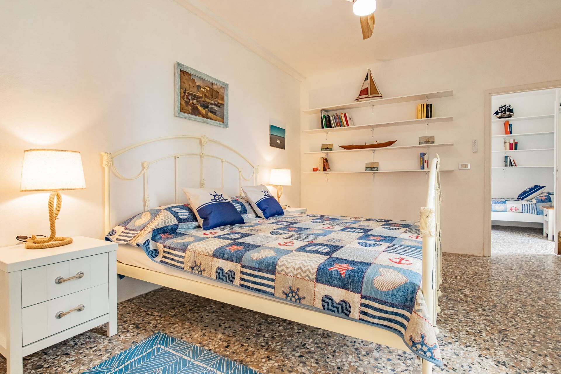 Une chambre à coucher bien rangée, avec un lit, des tables de chevet, une bibliothèque et un tableau accroché au mur.