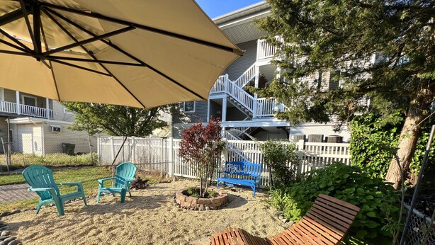 A patio with a wooden bench, two Adirondack chairs, and a large umbrella.