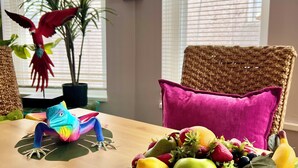 A dining table with a fruit bowl, a colorful parrot figurine, and a potted plant.