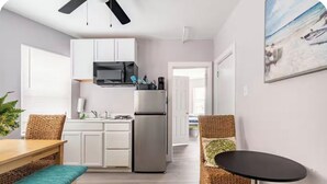 A modern kitchen with white cabinets, a stainless steel refrigerator, and a microwave. There is a dining area with a wooden table and wicker chairs.