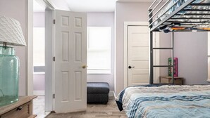 A bedroom with a bunk bed, a bedside table, a lamp, a window, and a door.