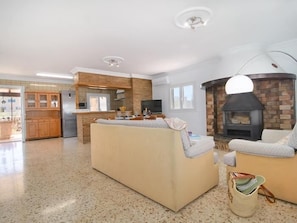 A spacious living area with a sofa, a fireplace, a kitchen area with wooden cabinets, and a television.