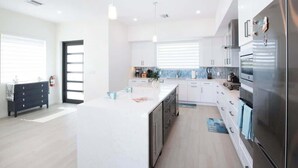 A modern kitchen with white cabinetry, stainless steel appliances, and a central island. - Oceanfront 3BR + Private Dock at Sea Haven – Cassava Point Villa 4D (Patricks Island)