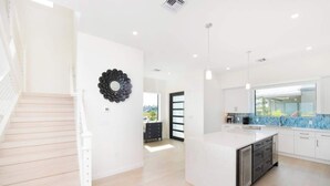 A modern kitchen with white cabinetry, a central island with a dishwasher, and a blue backsplash. - Oceanfront 3BR + Private Dock at Sea Haven – Cassava Point Villa 4D (Patricks Island)