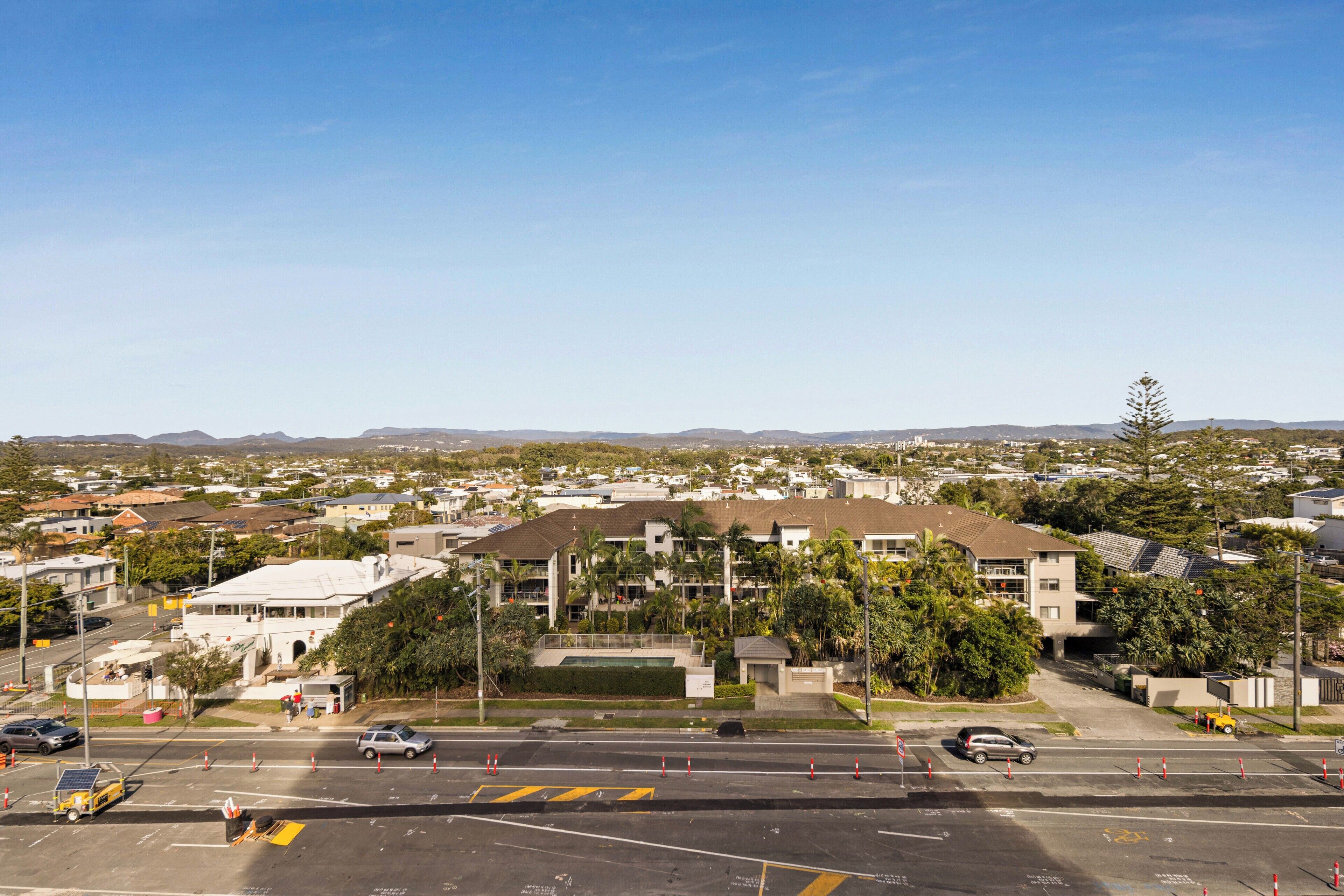 A multi-story building with a flat roof, surrounded by greenery and a clear sky.