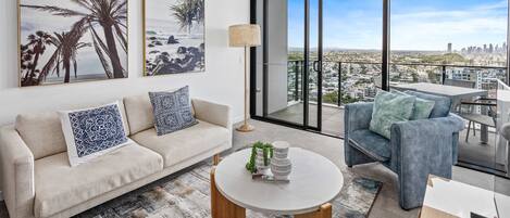 A modern living room with a sofa, a round coffee table, and a view of a cityscape through large windows.