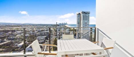A balcony with a white table and chairs, offering a city view.