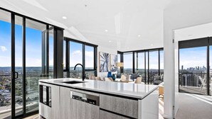 A modern kitchen with a large island, built-in dishwasher, and a city view through large windows. - Sandbar Burleigh Heads -Burleigh Letting (Burleigh Heads)