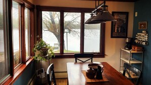En mysig matplats med ett träbord, stolar och en hängande lampa. En krukväxt står på fönsterbrädan och en inramad tavla hänger på väggen.