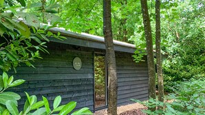 A small wooden cabin with a door and a sign, surrounded by dense green foliage.