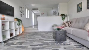 A modern living room with a sofa, a coffee table, and a TV on the wall. There is a kitchen area in the background.