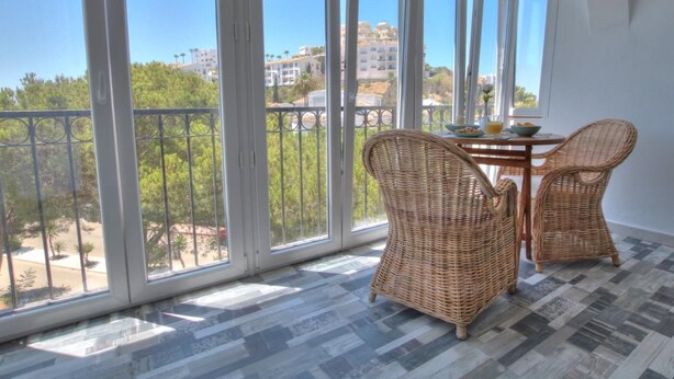 A balcony with large windows, wicker chairs, and a small table with a bowl and glass.