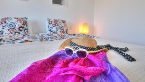 A bed with floral bedding, a woven hat, sunglasses, and a polka-dotted scarf on a white textured bedspread.