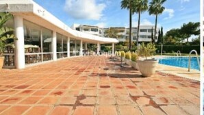 A hotel with a covered outdoor area, a swimming pool, and palm trees.