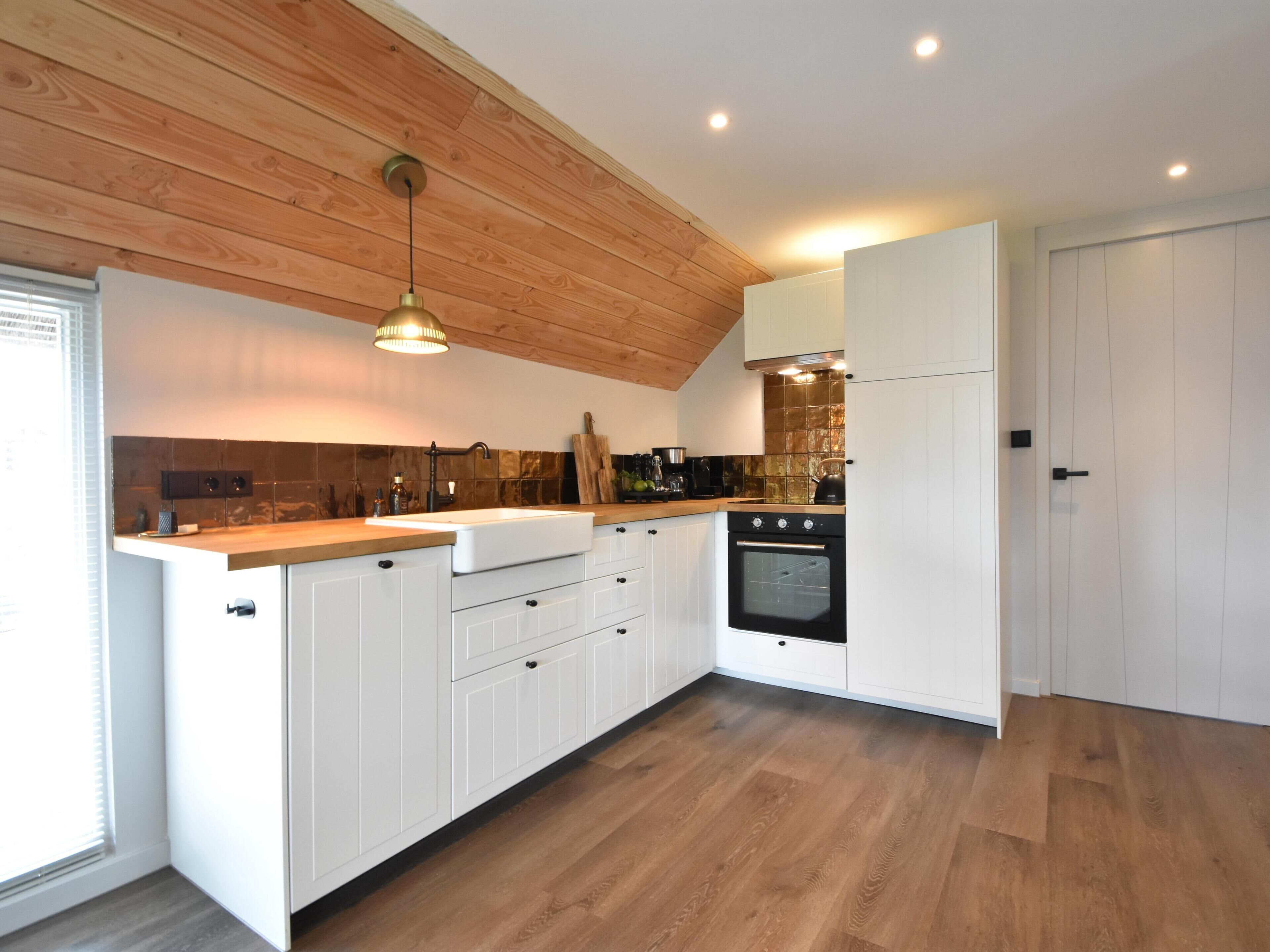 Una cocina moderna con armarios blancos, techo de madera y horno empotrado.
