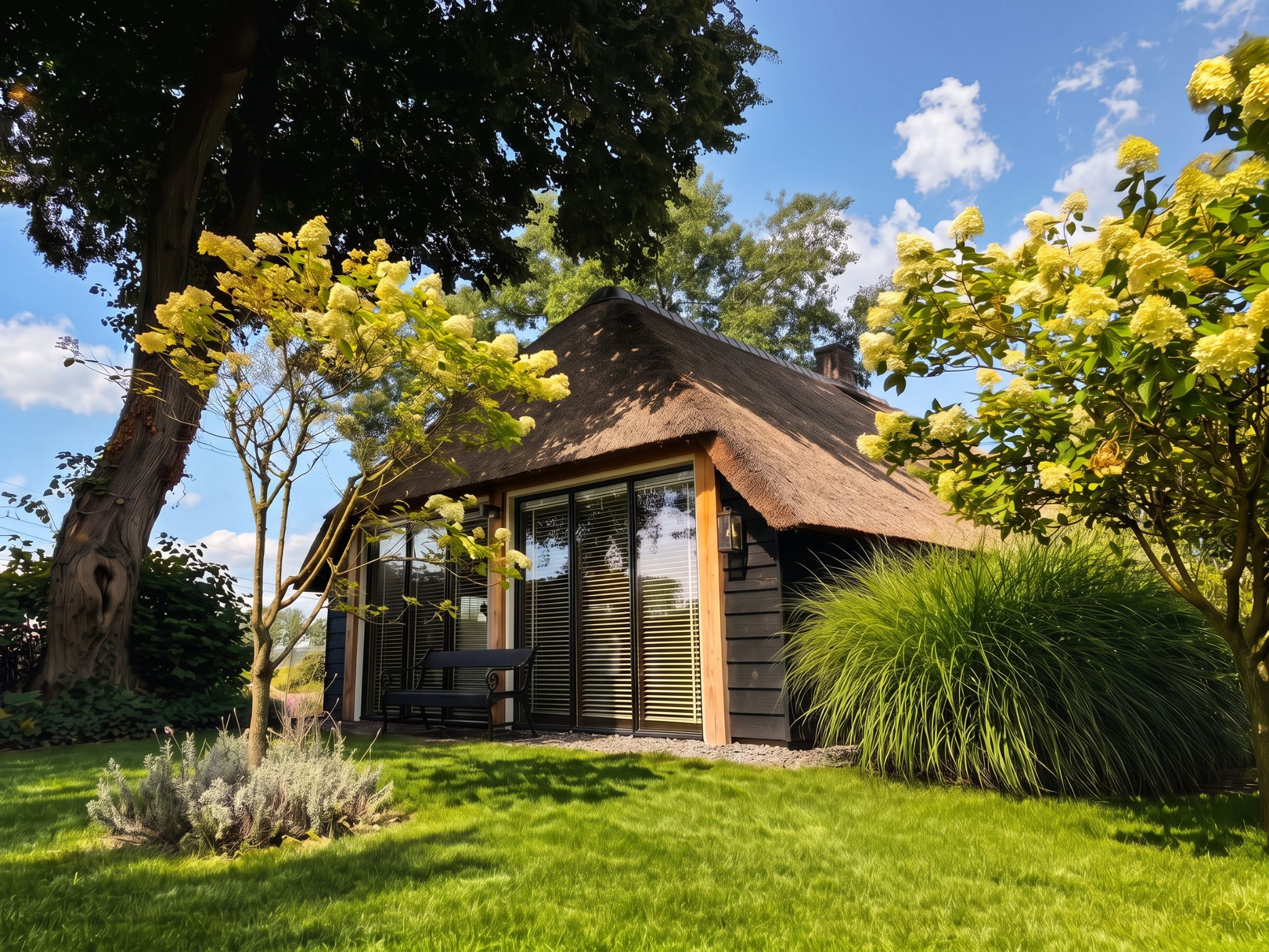 A thatched-roof cottage with a wooden exterior, surrounded by lush greenery and flowering trees.