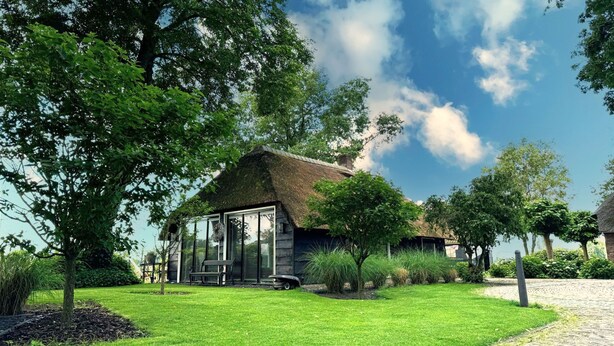 A rustic house with a thatched roof, surrounded by lush greenery and a cobblestone path.
