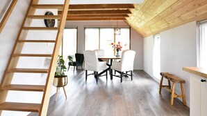 A modern interior with a wooden staircase, a dining area with chairs and a table, and large windows allowing natural light.