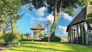A well-maintained garden with a thatched-roof structure, a wooden bench, and a clear sky.