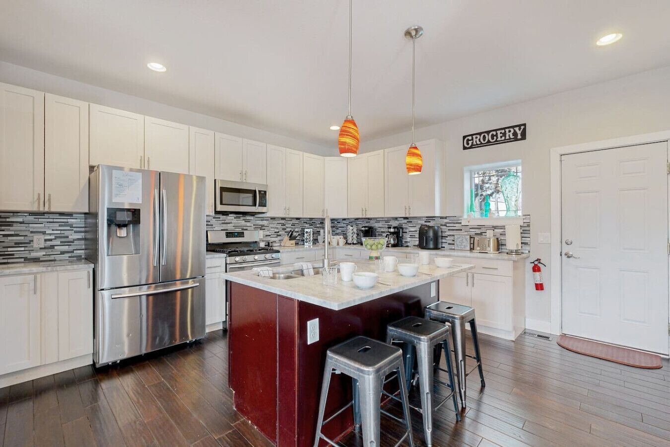 A modern kitchen with white cabinets, stainless steel appliances, a central island with stools, and pendant lighting.