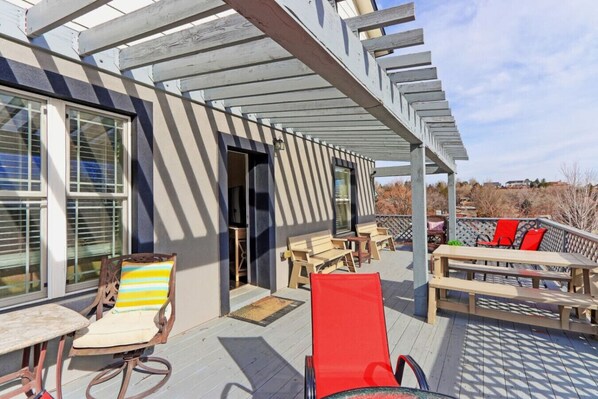 A covered outdoor deck with wooden furniture, including chairs and tables, and a view of the surrounding landscape.