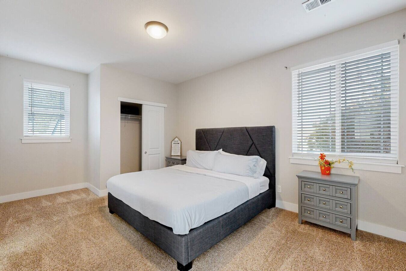 A bedroom with a bed, a dresser, a closet, and a window with blinds.