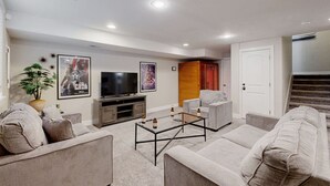Una sala de estar moderna con un televisor de pantalla plana, asientos cómodos, una mesa de centro y una escalera que lleva a otro nivel.
