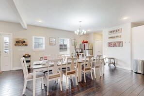 A dining area with a wooden table and chairs, a chandelier, and a refrigerator.