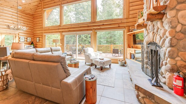 Ein geräumiges Blockhaus-Interieur mit großem Kamin, Ledersofas und einer Steinwand.