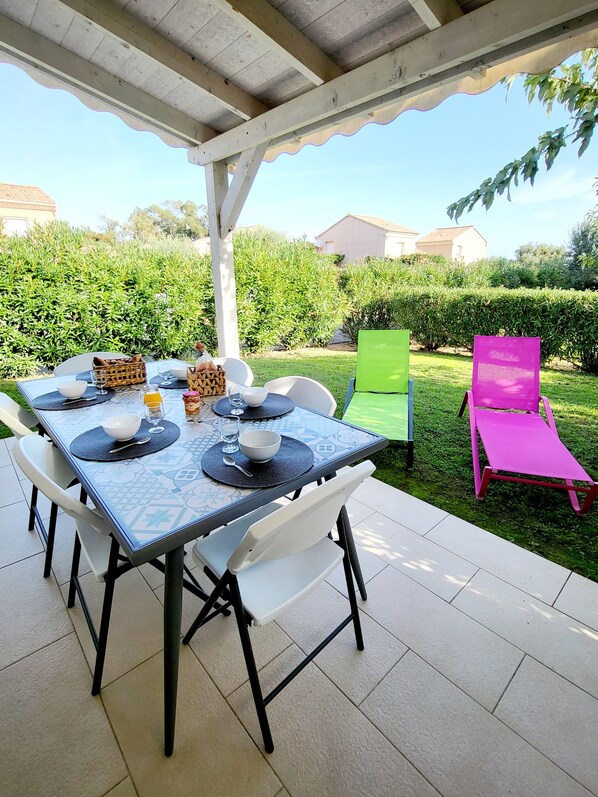 An outdoor patio with a table set for dining, surrounded by chairs and a pink lounge chair.