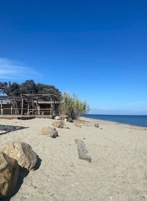 A beach with a wooden structure, large rocks, and a clear blue sky.