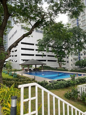 A swimming pool with lounge chairs, a gazebo, and a building with multiple floors in the background.